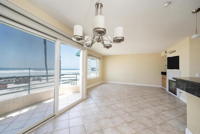 unfurnished dining area featuring a chandelier, a glass covered fireplace, light tile patterned floors, a water view, and baseboards