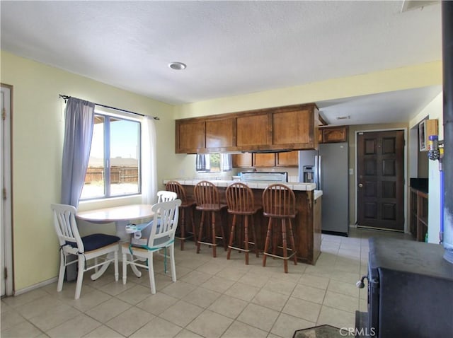 12981 Ojai Rd, Apple Valley, CA 92308 - kitchen with stainless steel fridge, a peninsula, brown cabinetry, a kitchen bar, and light countertops