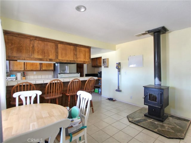 dining room with light tile patterned flooring, a wood stove, and baseboards