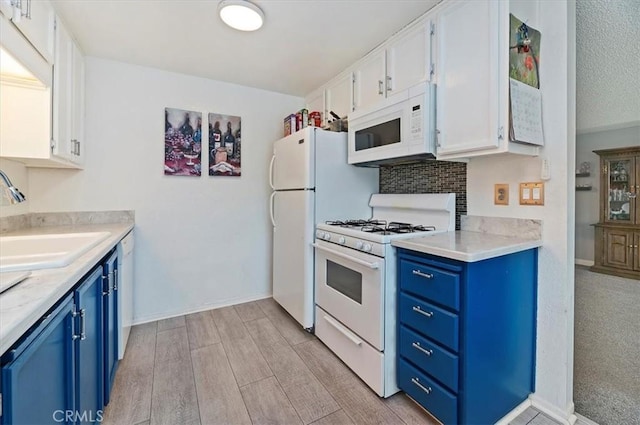 kitchen featuring white appliances, blue cabinets, a sink, white cabinetry, and light wood-style floors
