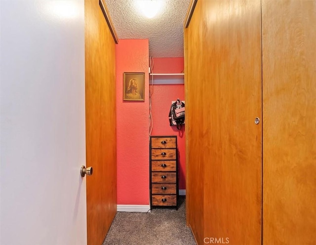 hallway featuring a textured ceiling, carpet flooring, baseboards, and a textured wall