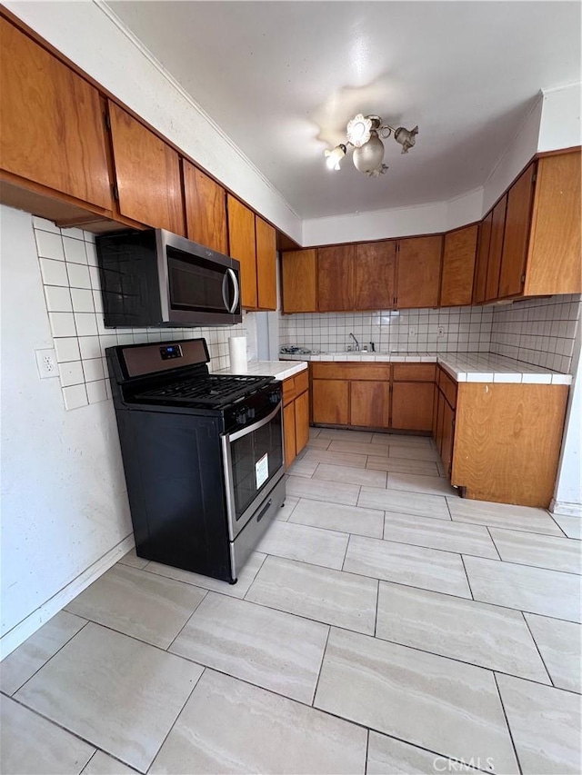 15407 S Visalia Ave, Compton, CA 90220 - kitchen with stainless steel appliances, brown cabinetry, backsplash, a sink, and tile countertops
