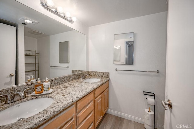 bathroom featuring baseboards, wood finished floors, and double vanity