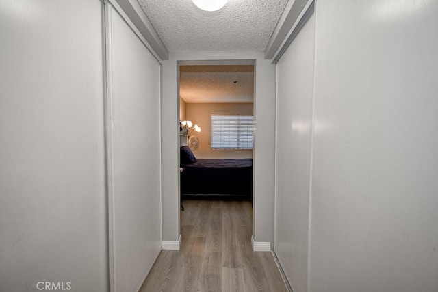 hall with a textured ceiling, wood finished floors, and baseboards