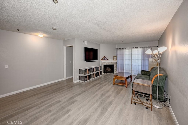 living area featuring light wood-style floors, a textured ceiling, baseboards, and a fireplace
