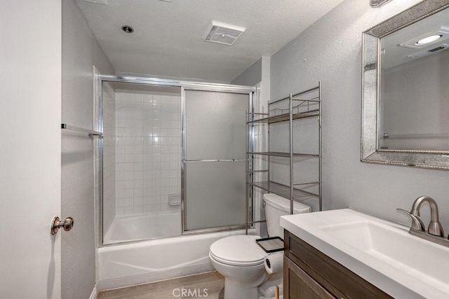 bathroom with toilet, a textured wall, vanity, bath / shower combo with glass door, and wood finished floors