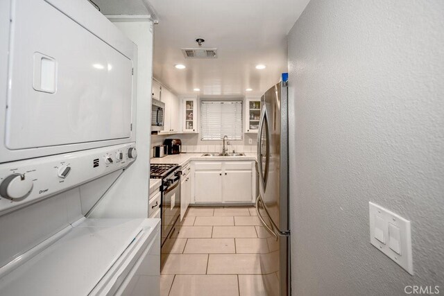kitchen featuring stainless steel appliances, a sink, stacked washing machine and dryer, light countertops, and white cabinetry