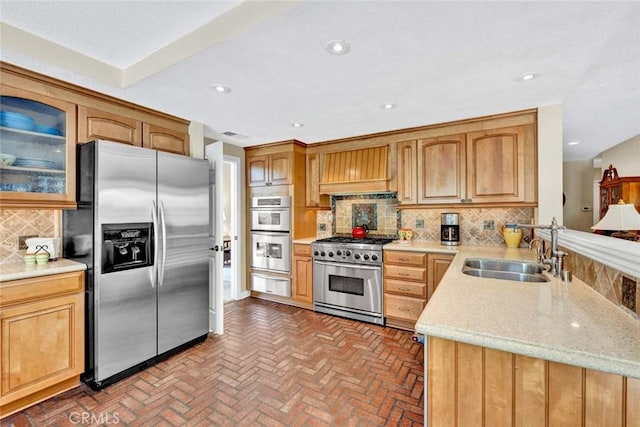 kitchen featuring appliances with stainless steel finishes, a sink, brick floors, a warming drawer, and premium range hood