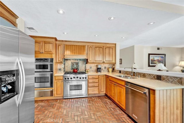 kitchen featuring stainless steel appliances, a sink, a warming drawer, light countertops, and a peninsula