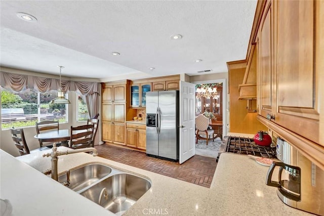 kitchen featuring stainless steel refrigerator with ice dispenser, a sink, glass insert cabinets, hanging light fixtures, and recessed lighting