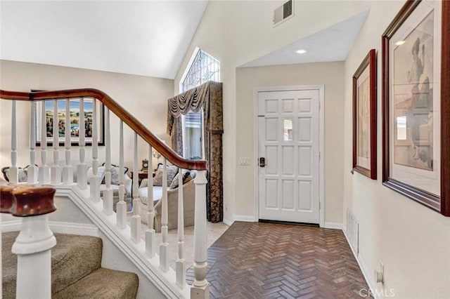 entryway featuring brick flooring, stairs, baseboards, and high vaulted ceiling