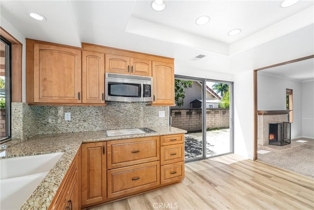 24752 Via, San Anselmo, Mission Viejo, CA 92692 - kitchen with stainless steel microwave, white electric cooktop, tasteful backsplash, a lit fireplace, and light stone counters