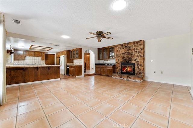 6367 Arrowhead Lake Rd, Hesperia, CA 92345 - unfurnished living room featuring ceiling fan, light tile patterned floors, arched walkways, a textured ceiling, and a stone fireplace