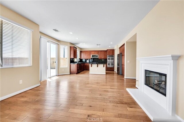 8 Via Del Fico Ct, Lake Elsinore, CA 92532 - unfurnished living room featuring a glass covered fireplace, light wood-style flooring, baseboards, recessed lighting, and a sink
