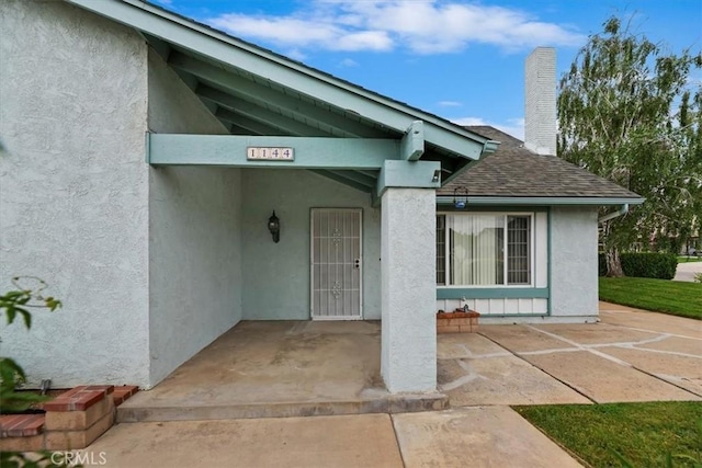 doorway to property featuring stucco siding, roof with shingles, and a chimney