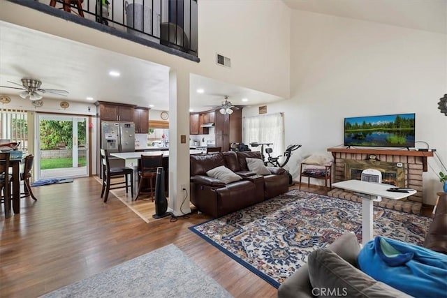 living room featuring ceiling fan, wood finished floors, a towering ceiling, a warm lit fireplace, and recessed lighting
