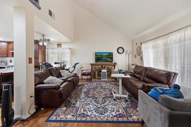 living room featuring wood finished floors, a ceiling fan, a brick fireplace, and high vaulted ceiling