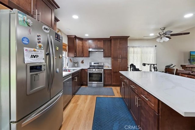 kitchen with stainless steel appliances, a sink, light wood-style flooring, under cabinet range hood, and ceiling fan