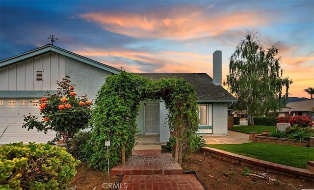 view of front of property with an attached garage, board and batten siding, a chimney, stucco siding, and a front lawn