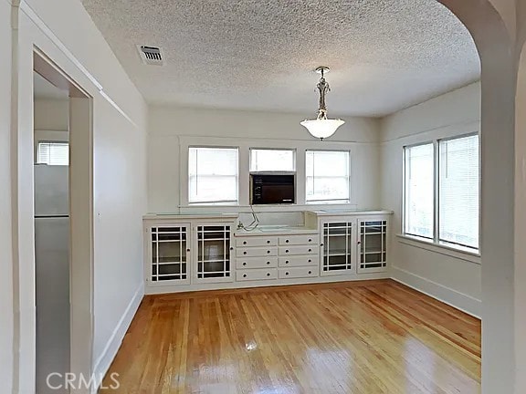 4890 7th Ave, Sacramento, CA 95820 - unfurnished dining area featuring light wood-style flooring, a textured ceiling, baseboards, and arched walkways