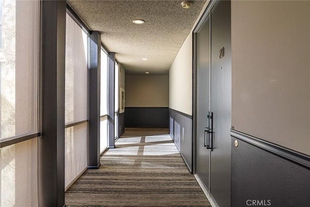 corridor featuring a textured ceiling, dark carpet, plenty of natural light, and recessed lighting