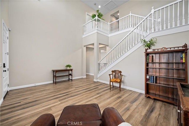 living area featuring a towering ceiling, stairway, wood finished floors, baseboards, and recessed lighting
