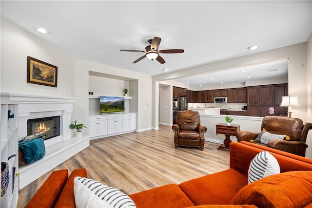 living room featuring ceiling fan, light wood-style floors, built in features, recessed lighting, and a glass covered fireplace