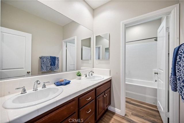 bathroom with wood finished floors, double vanity, baseboards, and bathing tub / shower combination