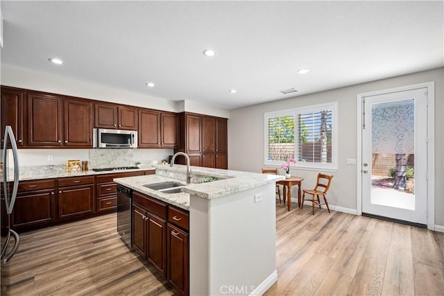 kitchen featuring stainless steel appliances, a sink, light wood finished floors, a center island with sink, and recessed lighting
