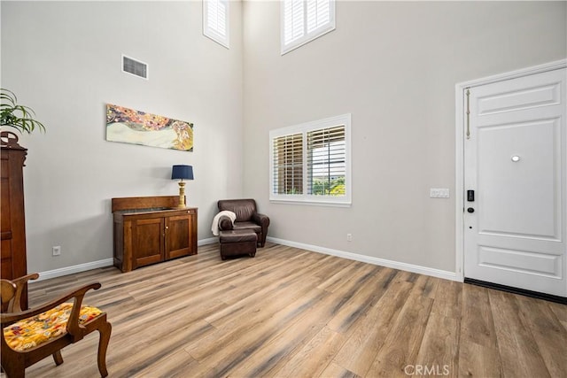 living area featuring a towering ceiling, plenty of natural light, light wood-style floors, and baseboards