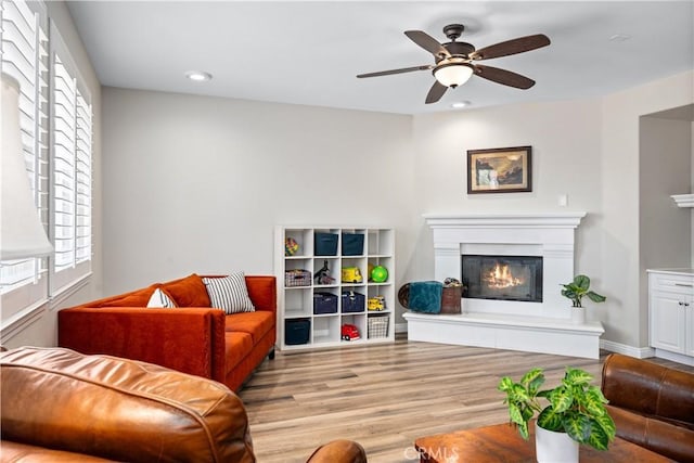 living area featuring a glass covered fireplace, wood finished floors, plenty of natural light, a ceiling fan, and recessed lighting
