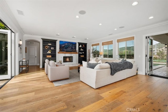 31740 Via Pamplona, San Juan Capistrano, CA 92675 - living room with crown molding, light wood-style floors, built in shelves, a glass covered fireplace, and arched walkways