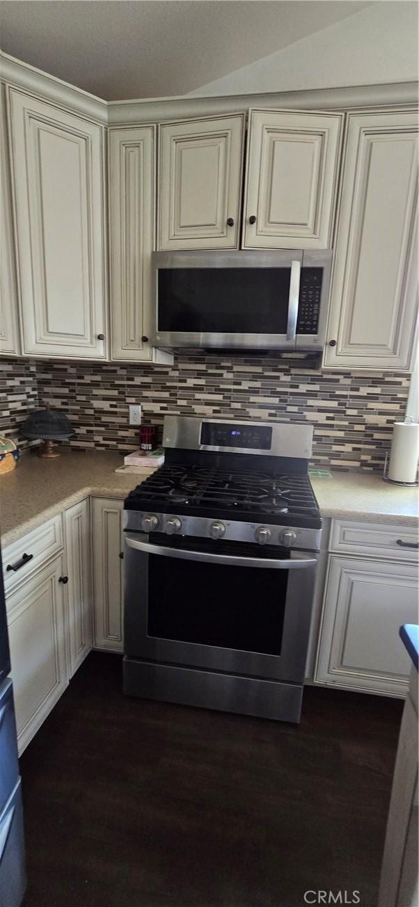 kitchen featuring appliances with stainless steel finishes, tasteful backsplash, light countertops, cream cabinets, and dark wood-style floors