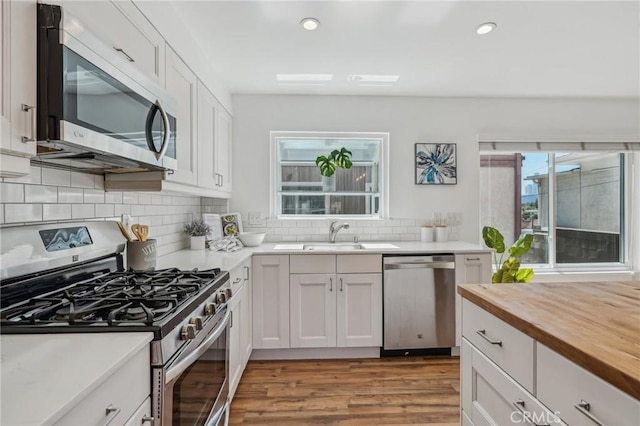 kitchen with stainless steel appliances, wood counters, a sink, light wood-type flooring, and recessed lighting