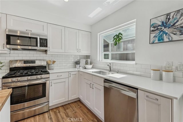 kitchen with appliances with stainless steel finishes, decorative backsplash, white cabinets, and light wood finished floors