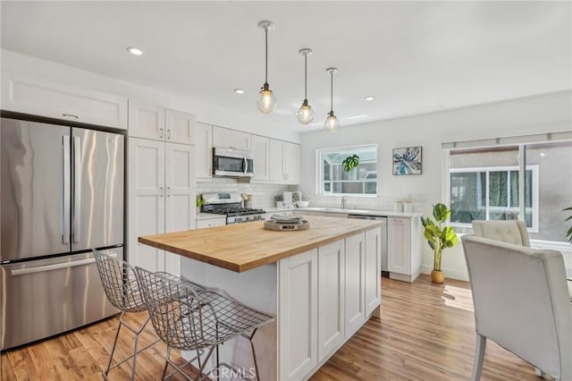 kitchen with stainless steel appliances, butcher block countertops, white cabinetry, plenty of natural light, and recessed lighting