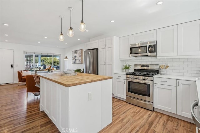 kitchen featuring stainless steel appliances, butcher block counters, light wood-style floors, decorative backsplash, and recessed lighting