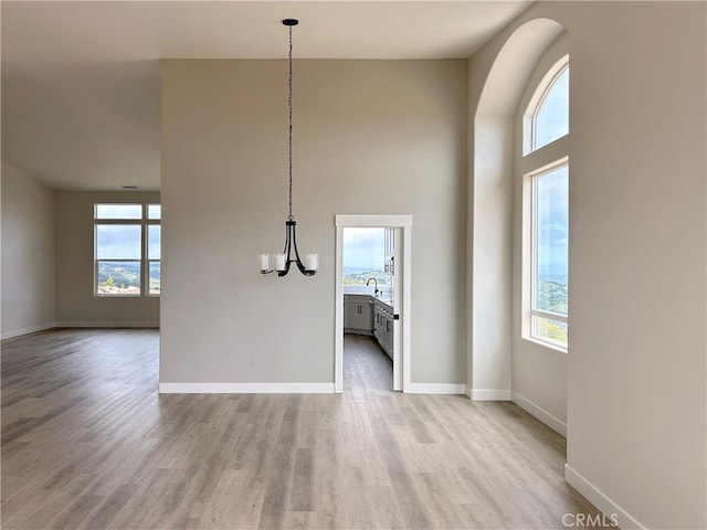 unfurnished dining area with light wood-style floors, a chandelier, baseboards, a sink, and a high ceiling