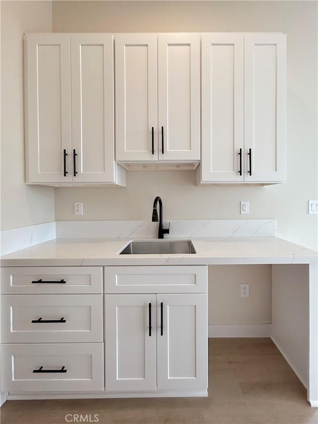 kitchen featuring a sink, light stone counters, white cabinets, light wood-type flooring, and baseboards