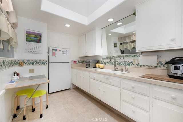 kitchen featuring freestanding refrigerator, a sink, light countertops, white cabinetry, and recessed lighting