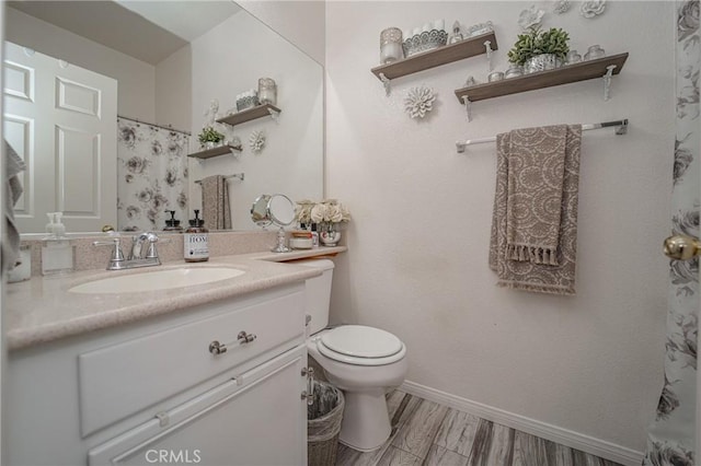 full bath with toilet, vanity, wood finished floors, and baseboards
