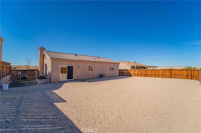 back of house featuring a tiled roof, stucco siding, cooling unit, a chimney, and a fenced backyard