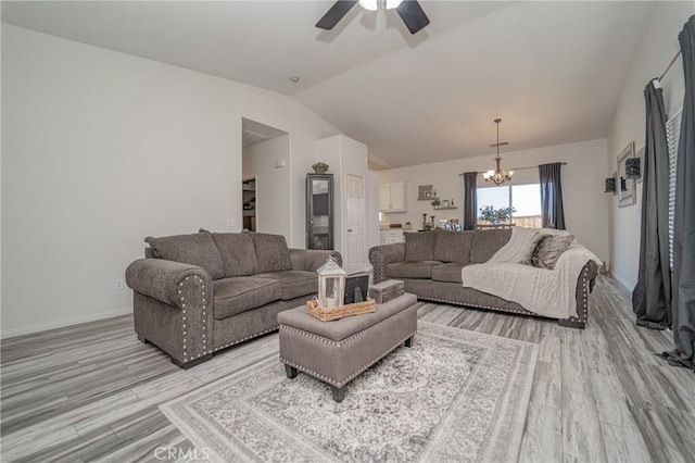 living area with lofted ceiling, a chandelier, light wood-style floors, ceiling fan, and baseboards