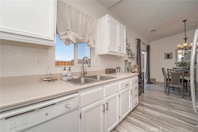 kitchen with a sink, white dishwasher, a chandelier, white cabinetry, and light countertops
