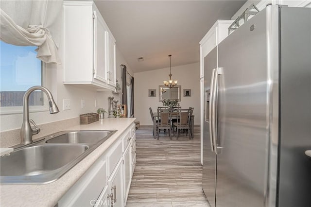 kitchen featuring stainless steel refrigerator with ice dispenser, a sink, a chandelier, white cabinets, and light countertops