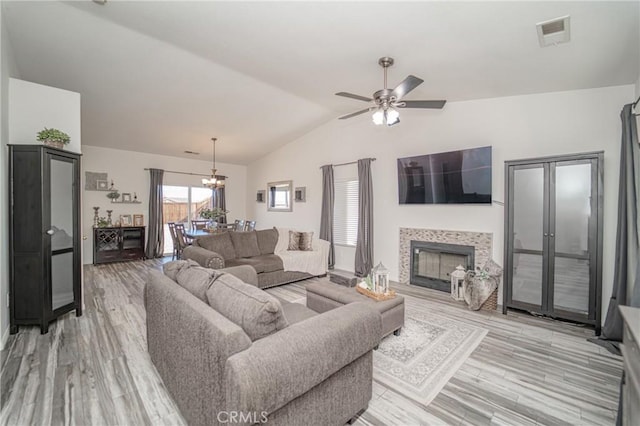 living area with vaulted ceiling, a tile fireplace, light wood-style flooring, a ceiling fan, and a chandelier