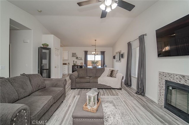 living room featuring vaulted ceiling, a chandelier, light wood-style flooring, ceiling fan, and a fireplace