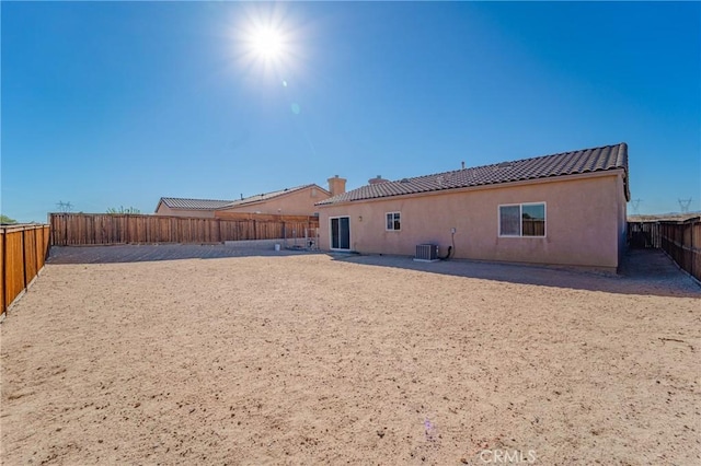rear view of house featuring stucco siding, a tiled roof, central AC, a fenced backyard, and a chimney