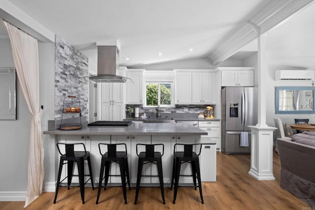 kitchen with stainless steel fridge, island range hood, a wall mounted AC, a sink, and lofted ceiling