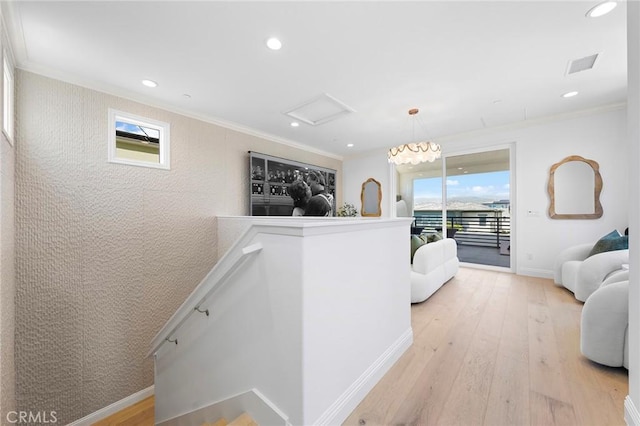 corridor with an upstairs landing, ornamental molding, light wood finished floors, baseboards, and attic access